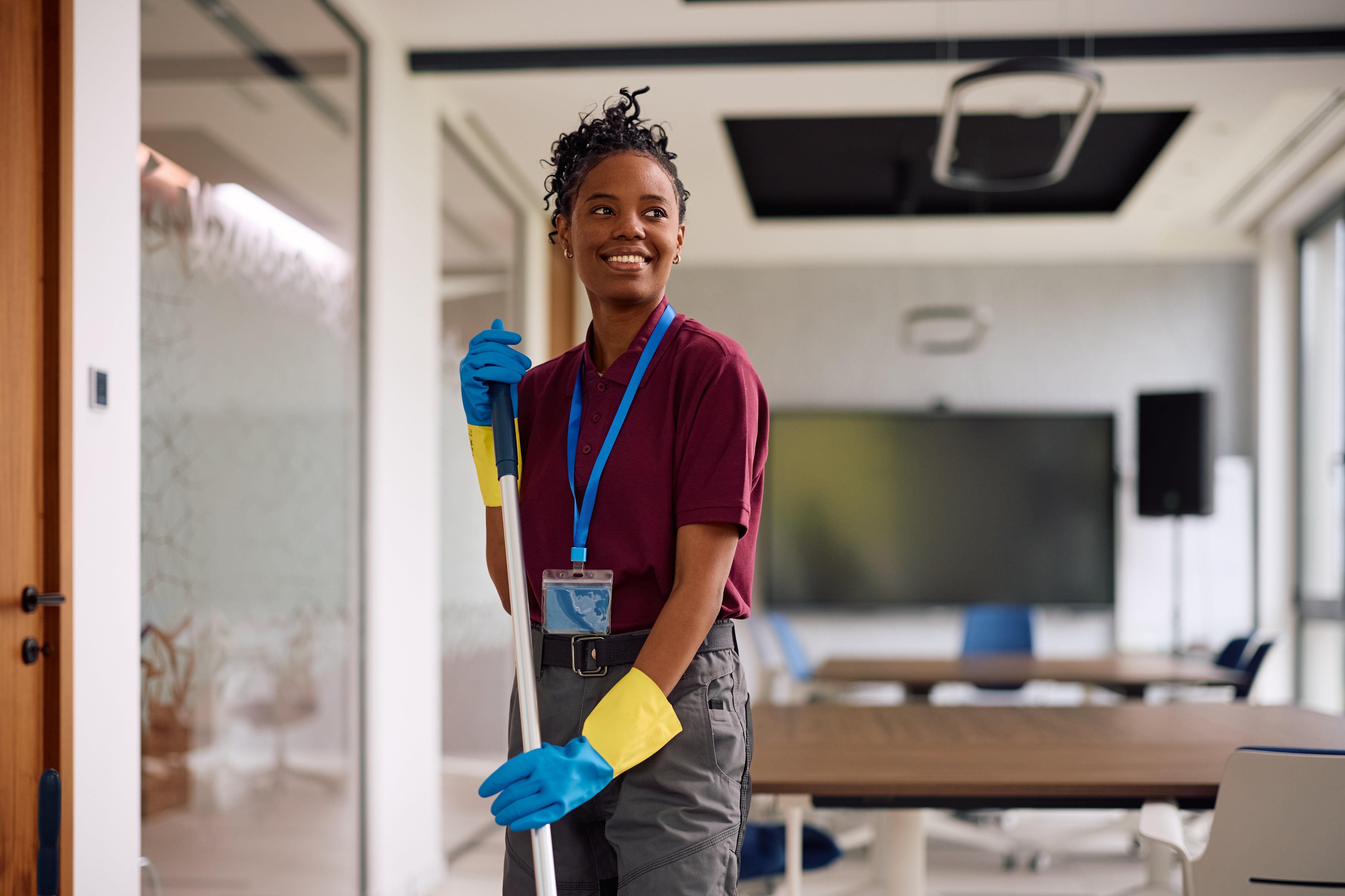 Happy African American professional cleaner cleaning an office building interior. Copy space.